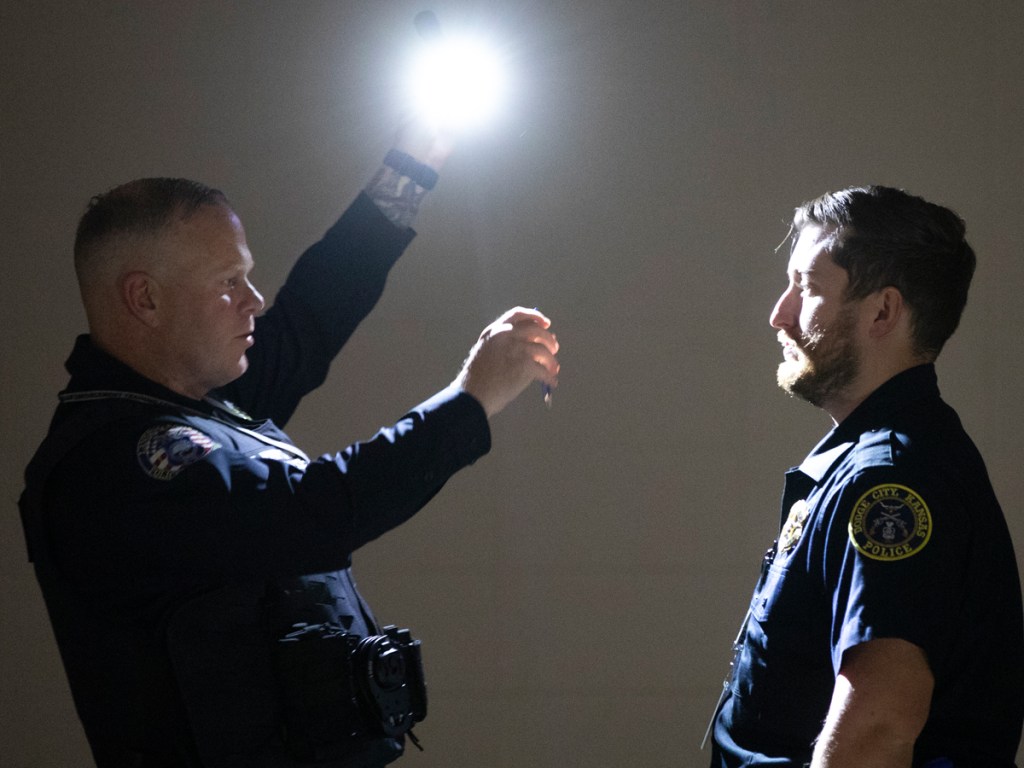 Police officer shining flashlight in the face of fellow officer.